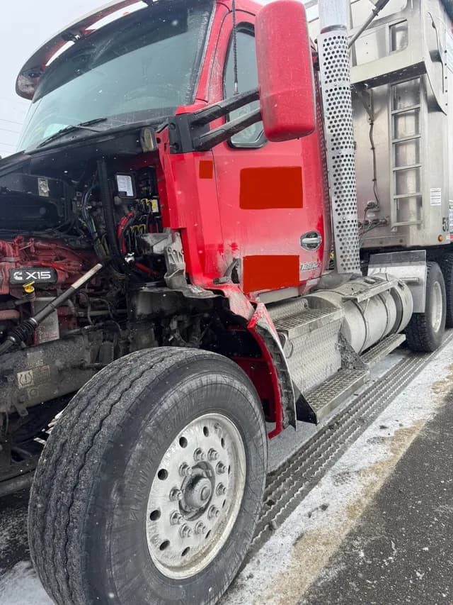 Red Kenworth T880 with cab tilted forward exposing the Cummins engine in snow
