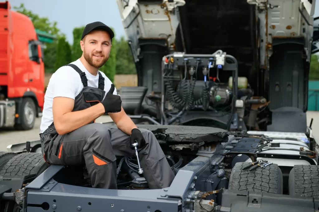 A caucasian mechanic giving a thumbs up while sitting at the back of the trailer truck