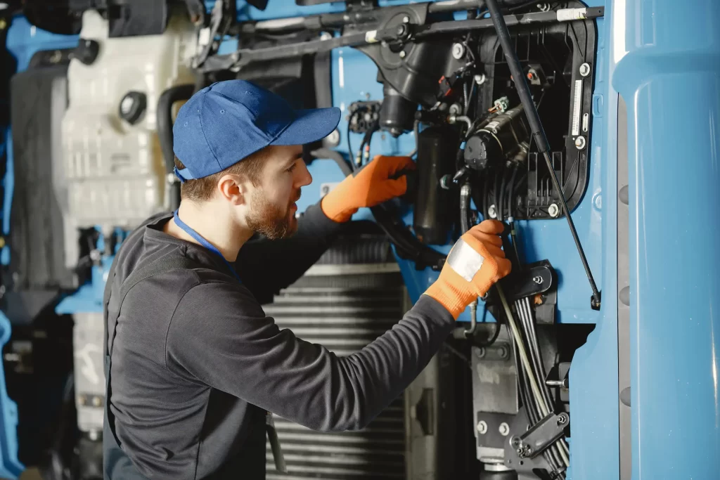 an image of a mechanic checking the wires at the front hood of the trailer truck