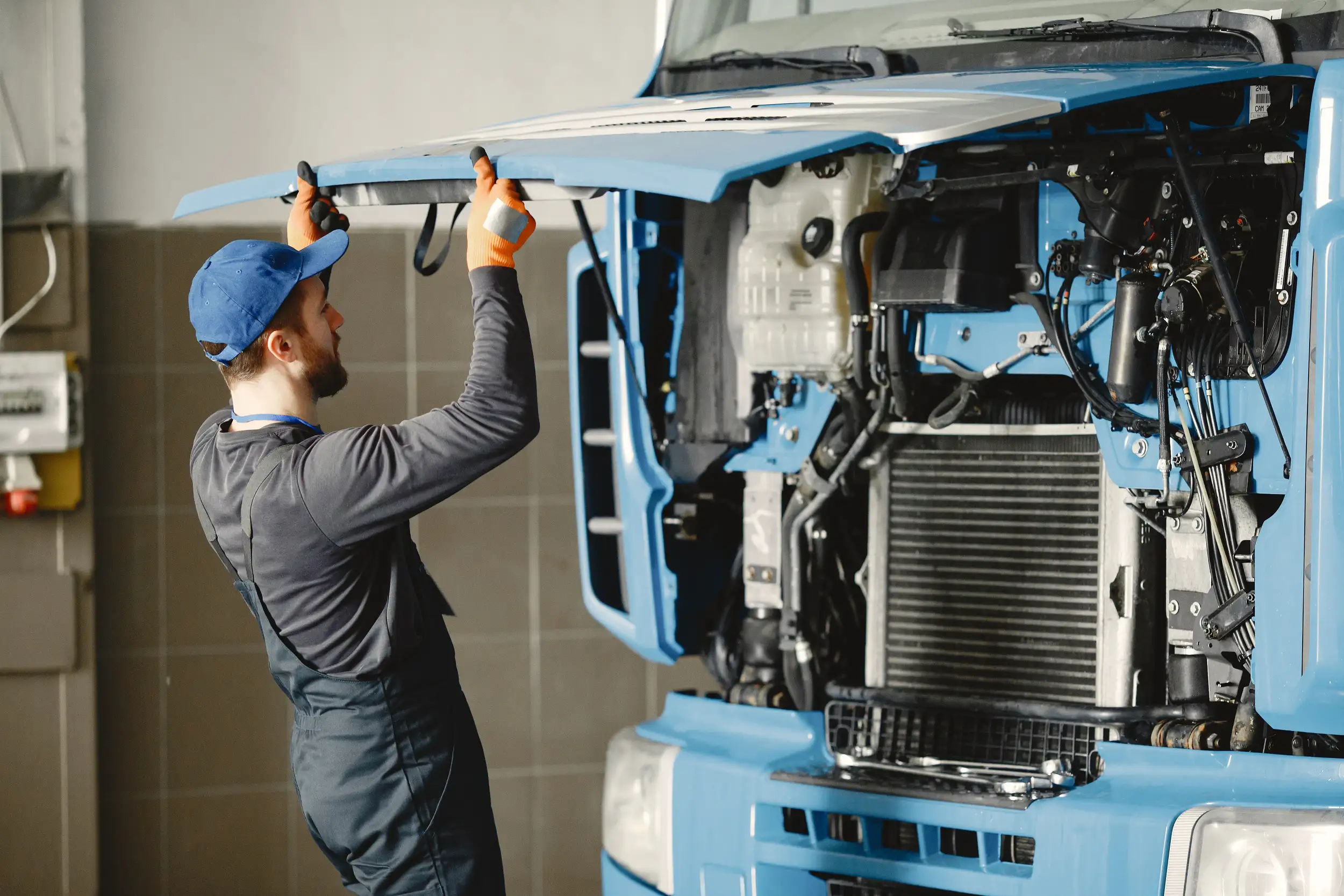 A mechanic in uniform opening the hood of the trailer truck