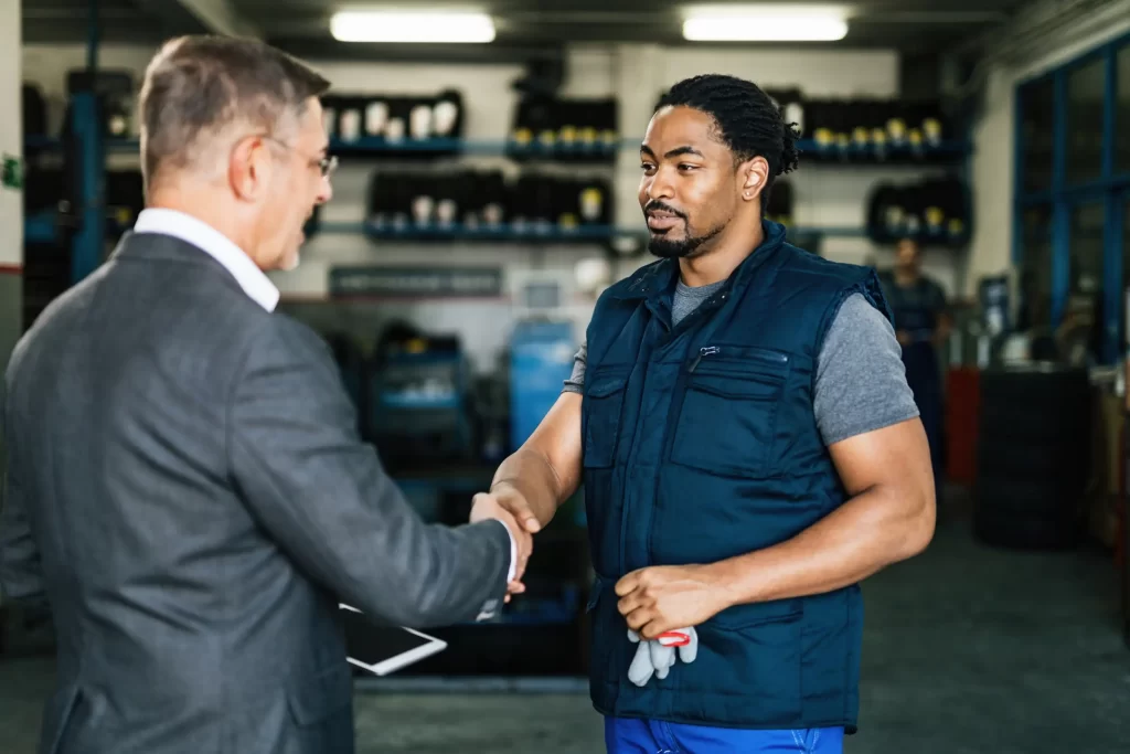 Fleet maintenance partnership with a mechanic and a manager shaking hands in a workshop.